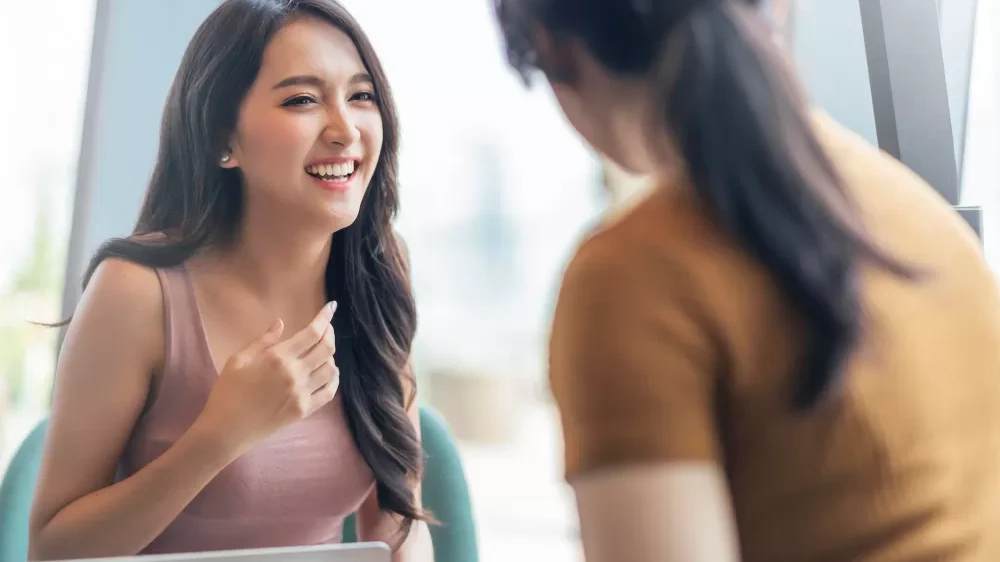 A woman engages in conversation with another during a meeting, discussing preparations for a successful first day at work. 