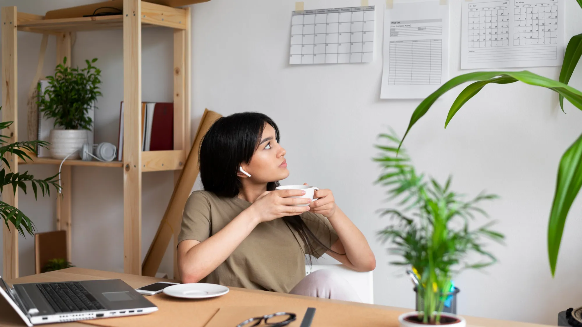 A woman seated at a desk, working on a laptop while enjoying a cup of coffee, preparing to send her CV on Sunday.