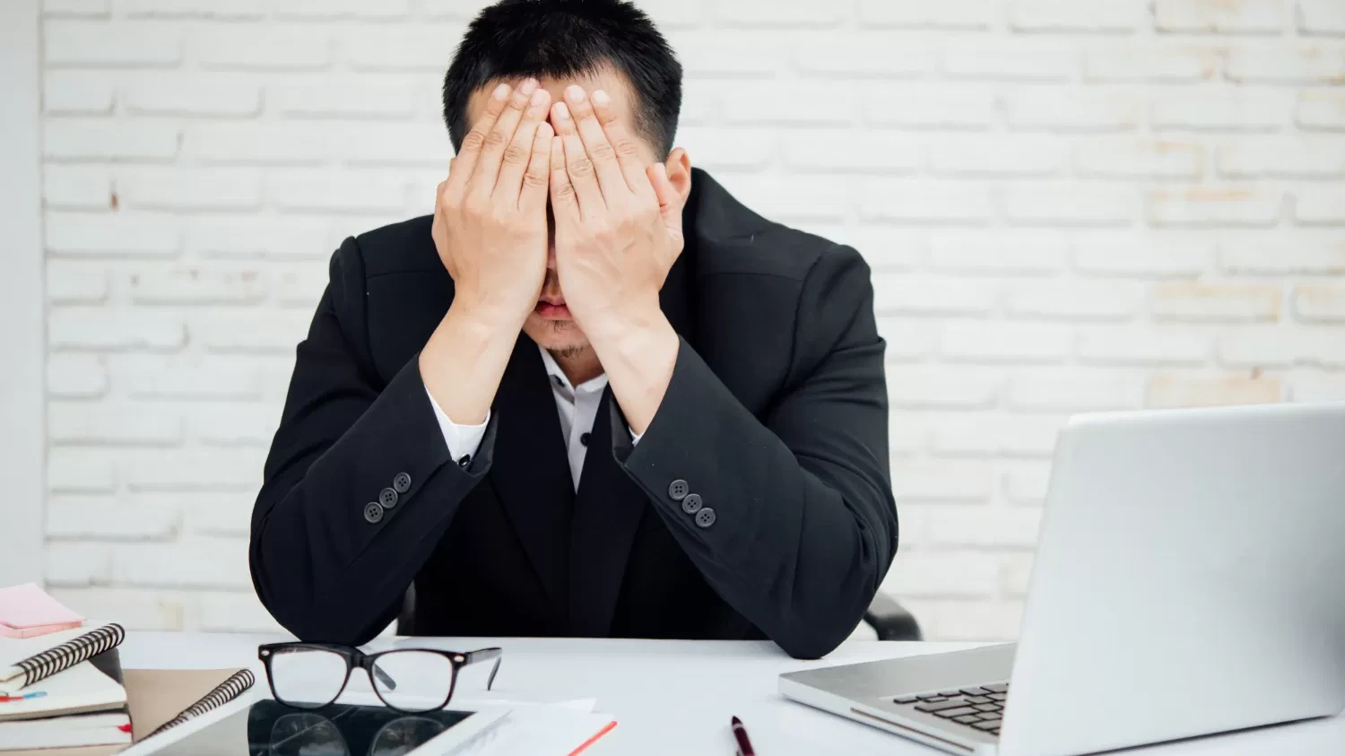 A man in a suit sits at his desk, hands on his face, contemplating reasons for not receiving a promotion.